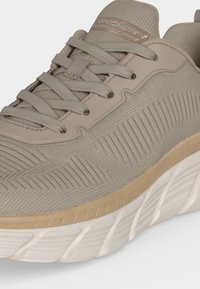 Baskets Skechers beige clair avec tige en maille, languette rembourrée, lacets assortis, design texturé et semelle blanche amortissante.