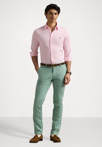Vaaleanpunainen pitkähihaisen napitettava paita, mintunvihreät slim-fit housut, ruskea vyö ja loafers-kengät. Paidassa on logo.