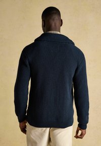 Navy blaues, geripptes Strickpullover mit Schalkragen, lange Ärmel und strukturiertem Stoff. Die Rückansicht zeigt eine figurbetonte Silhouette.