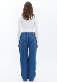Jeans de mezclilla azul de pierna ancha con una cintura alta, que cuentan con dos bolsillos traseros y costuras en contraste sutiles. Tejido suave y texturizado, ajuste casual.