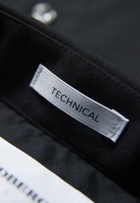 Zwarte stof met een geweven textuur heeft een wit label met de tekst "TECHNICAL." Het label is met nette randen genaaid.
