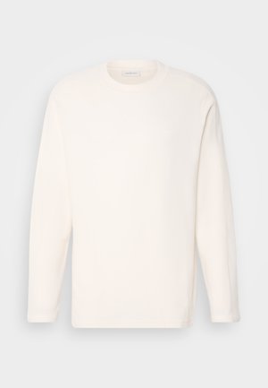 Långärmad tröja med rund hals i off-white tyg med en slät textur. Diskret logotypdetalj på bröstet, rak nederkant och mjuka manschetter.
