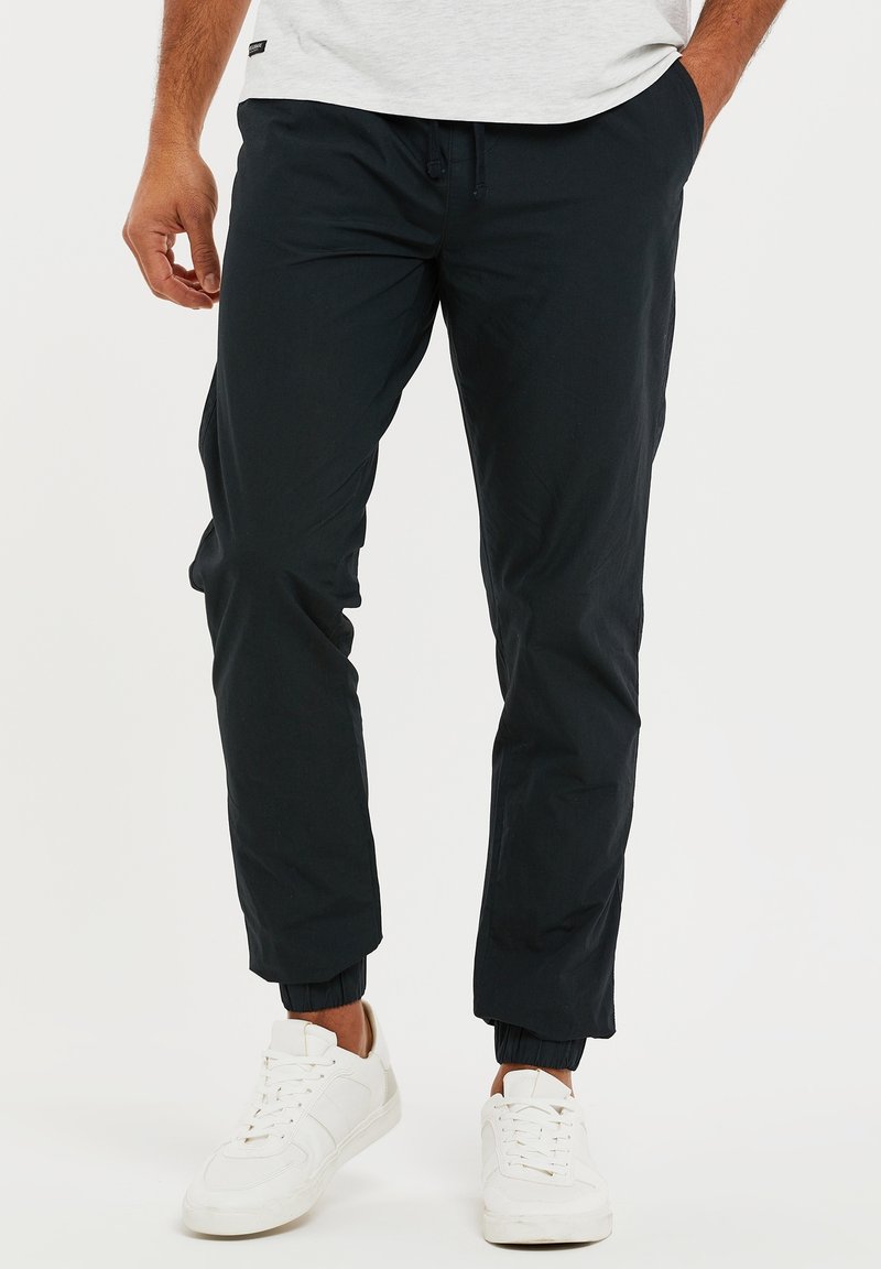 Marineblauwe joggingbroek met elastische manchetten, een trekkoordtailleband en een gladde textuur. Gemaakt met witte sneakers.