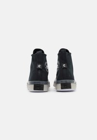 Schwarze Canvas-Ankelboots mit einer strukturierten oberen Fläche, transparenter Gummisohle und Logo-Akzenten an der Ferse und der Seite. Sie verfügen über Ziehschlaufen für einfaches Anziehen.