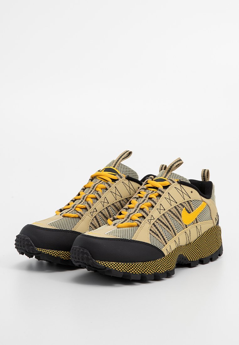 Beżowo-czarne buty sportowe z żółtymi akcentami, siateczkowa i syntetyczna cholewka, teksturowana gumowa podeszwa oraz charakterystyczny wzór po bokach.