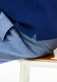 Marineblauw top met een gestructureerde afwerking,laag over lichtblauwe denim broek met een zijzak, rustend op een houten oppervlak.