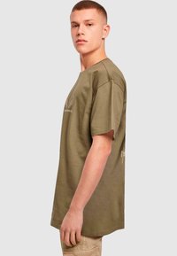 Olive green cotton t-shirt with a relaxed fit, short sleeves, and a subtle graphic design on the front, featuring a crew neckline.