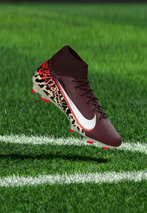 Bordo nogometni čevelj z belim Nike črtom in rdeče-črnim živalskim vzorcem, ki lebdi nad zeleno travo blizu bele mejne črte na igrišču.