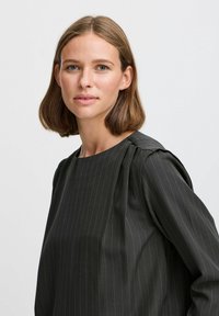 Blusa grigia scura con righe verticali, maniche a sbuffo e scollatura arrotondata. Tessuto liscio con leggero lucido e dettagli di cucitura delicati.