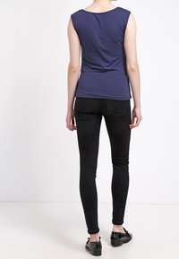 Marinblå ärmlös topp med rund halsringning, kombinerad med svarta slim-fit jeans och svarta ballerina skor, sedd bakifrån mot en neutral bakgrund.