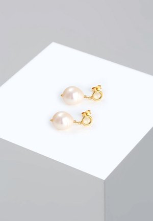 Paar goldene Ohrstecker, jeweils mit einer einzelnen runden weißen Perle, präsentiert auf einem weißen geometrischen Sockel vor grauem Hintergrund.