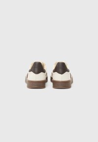 Sneaker in pelle bianca e marrone, con una suola in gomma marrone texturizzata, punta arrotondata e dettagli marroni a contrasto sul tallone.