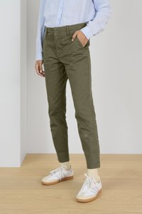 Olivgrön, slim-fit bomullsbyxor med sidofickor och en slät yta, tillsammans med vita sneakers och ljusa strumpor.