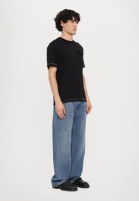 Svart kortermet t-skjorte med kontraststing, kombinert med løstsittende lyseblå jeans og svarte kraftige sko.