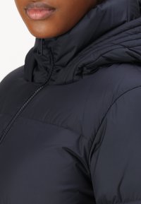 Laivastonsininen toppatakki, jossa on korkea kaulus ja vetoketjusuljenta, valmistettu sileästä, vedenkestävästä materiaalista ja tikatulla tekstuurilla.