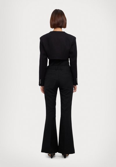 Fekete, crop fazonú blazer struktúrált vállakkal egy testhezálló fekete topp felett, magas derekú fekete, kinyíló nadrággal párosítva, sima textúrával és precíz szabással.