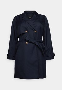 Trench coat di colore blu navy con parte frontale doppiopetto, bottoni dorati, cintura in vita e polsini arrotolati; realizzato in tessuto liscio con un design sartoriale.