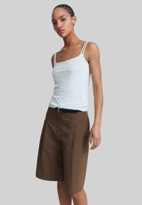 White sleeveless top with thin straps paired with brown knee-length shorts featuring a belt, both made of smooth fabric.