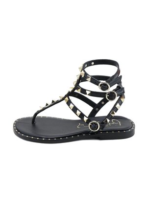 Sandalia plana negra con tres tiras ajustables con hebilla y tachuelas piramidales doradas a lo largo de las tiras y el borde de la suela.