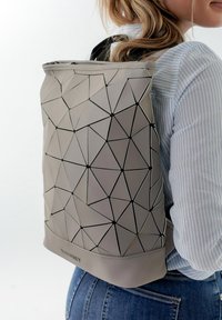Pilkas geometrinio rašto kuprinė su tekstūruota paviršiumi ir juodais akcentais. Turi ritininį uždarymą ir reguliuojamas petnešas.