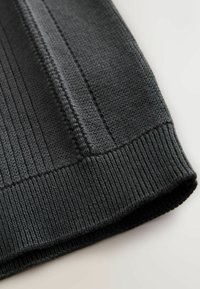 Mørkegråt strikket stof med teksturerede striber og ribbet kant. Materialet virker blødt med et ensartet mønster gennem hele stoffet.