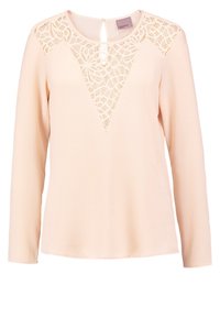 Blouse à manches longues couleur pêche avec un tissu texturé, comprenant un motif ajouré en dentelle en forme triangulaire sur le devant et un détail en forme d'œillet au dos.