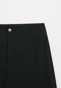 Pantalon noir taille haute avec fermeture à un seul bouton, couture avant visible et tissu lisse sur un fond neutre.