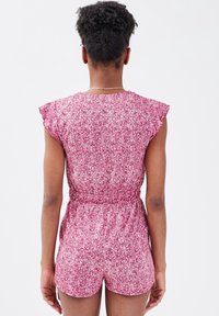 Floraler Jumpsuit in Pink mit tailliertem Schnitt, kurzen Ärmeln und Rüschendetails. Der Stoff zeichnet sich durch ein strukturiertes, mehrfarbiges Muster aus.