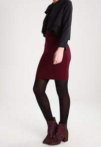 Černý zkrácený top, burgunský bodycon šaty, černé neprůhledné punčocháče a vzorované kotníkové boty v odstínech fialové a hnědé.