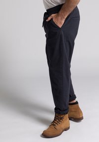 Pantalones de cintura elástica azul marino con bolsillos laterales, presentan un diseño ajustado. Combinados con botas de ante marrón con cordones.