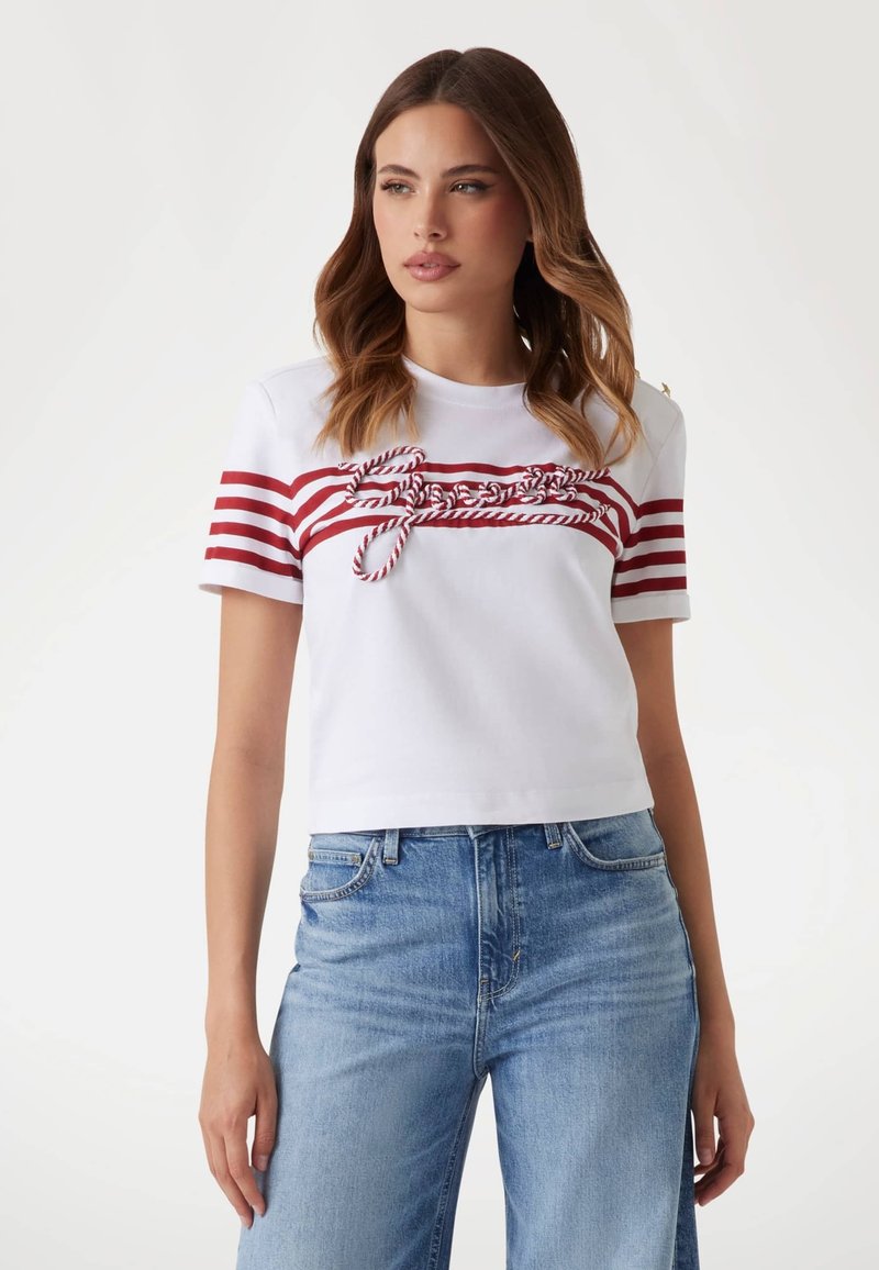 Witte cropped t-shirt met rode horizontale strepen en een geknoopt detail over de borst. Gecombineerd met lichtblauwe denim jeans.