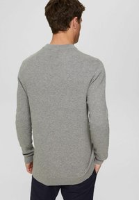 Šedý pletený svetr s dlouhými rukávy, kulatým výstřihem a ribbovanými manžetami. Má strukturovaný vzor a mírně zakřivený lem.