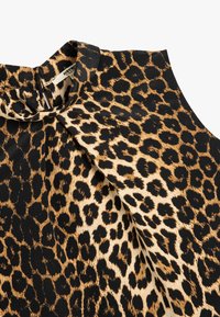 Blusa con stampa leopardata caratterizzata da una combinazione di colori nero e beige, tessuto morbido e design del collo plissettato.