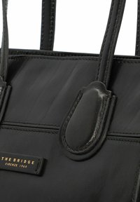Borsa a mano in pelle nera caratterizzata da una superficie liscia, dettagli di cucitura e una placca logo dorata con la scritta "THE BRIDGE, FIRENZE 1969."
