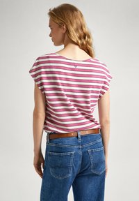 Dryžuota rožinė ir pilka marškinėliai, trumpomis rankovėmis, apvaliu iškirpimu, derinami su mėlynomis džinsomis, turinčiomis rudą diržą ir dekoratyviais kišenių siuvinėjimais.