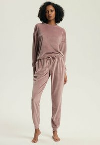 Jasnoróżowy, miękki zestaw dresowy z weluru. Bluzka z długim rękawem o luźnym kroju oraz spodnie jogger z elastycznym pasem i mankietami.