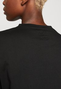 T-shirt in cotone nero con scollatura rotonda e un design ricamato discreto sulla parte superiore della schiena. Texture liscia, design aderente.