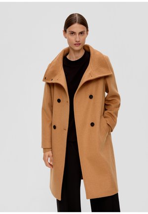 Manteau camel croisé avec un large col, fabriqué en laine texturée, avec des boutons noirs et des poches latérales, porté sur un haut noir.