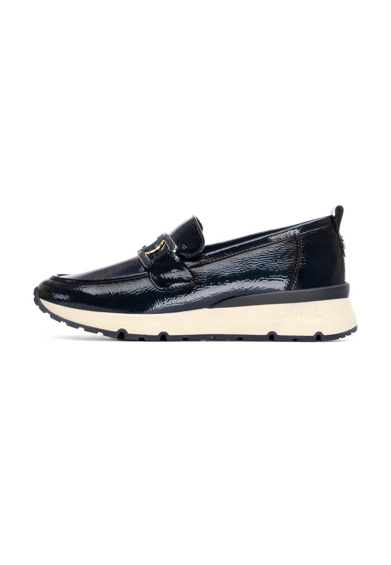 Zapato negro de charol sin cordones con un acento de hebilla, parte superior texturizada, punta curvada y una suela de goma crema en contraste.