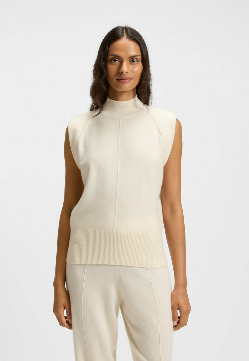 Knit sleeveless top in off-white with a high collar, ribbed hem, and smooth texture. Features minimalist design and subtle seam detailing.
