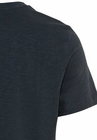Gros plan sur un T-shirt noir texturé à manches courtes montrant le dos et l'épaule droite.