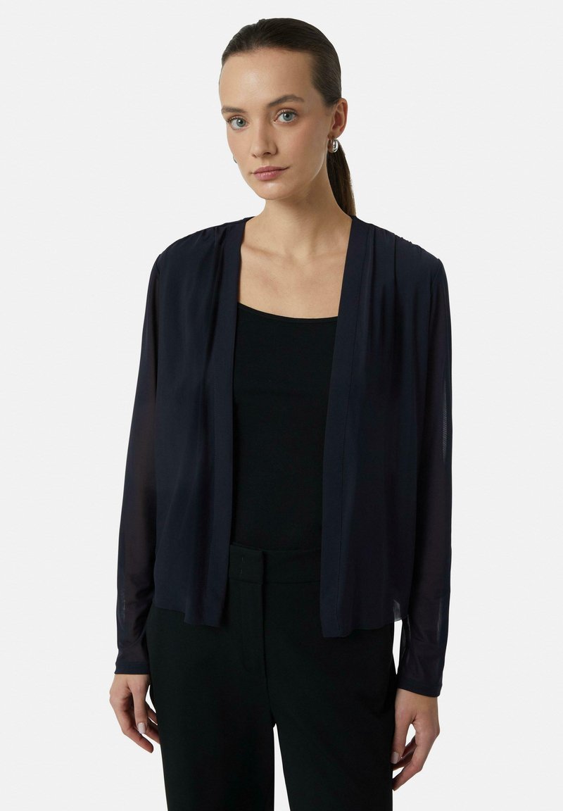 Lekki, granatowy, przezroczysty kardigan z otwartym przodem i długimi rękawami, założony na czarny top na ramiączkach i spodnie. Gładka tekstura, zwiewny fason.