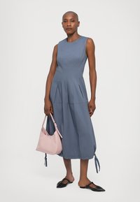 Mėlyna be rankovių suknelė su klostuotu sijonu, tekstūruota medžiaga ir raišteliu apatinėje dalyje. Derinama su rožine rankine ir juodomis butais.