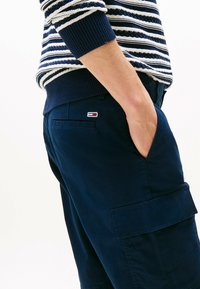 Granatowe szorty cargo z bocznymi kieszeniami, wykonane z gładkiego materiału. Połączone z swetrem z dzianiny w paski z niebieskimi, białymi i czerwonymi akcentami.