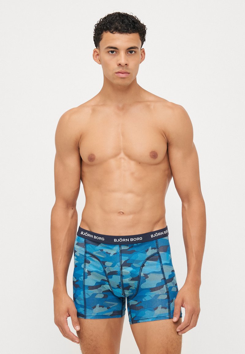 Blaue Camouflage-Boxershorts mit schwarzem Bund, der das Logo "BJÖRN BORG" zeigt. Hergestellt aus elastischem Material, das eine enge Passform und eine glatte Textur bietet.