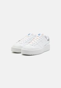 Vita atletiska sneakers med en slät läderöverdel, rund tå, framträdande snören och en tjock, texturerad sula. Ljusblå accenter på tungan.