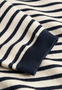 Nahaufnahme eines cremefarbenen und marineblau gestreiften Strickstoffs mit einem gerippten navyblauen Bündchen, das Textur und Muster hervorhebt.