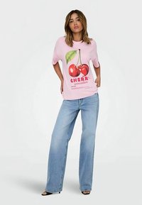 Lyserød T-shirt med kirsebærmotiv og tekst, sat sammen med lyseblå vidde buks. Stoffet virker blødt med en afslappet pasform.