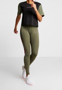 Svart och olivgrön träningskläderset bestående av en croppad t-shirt och högmidjade leggings med sidodetaljer och logotyp. Strukturerad tyg.