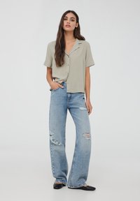 Camicetta grigia chiara a maniche corte con bottoni abbinata a jeans larghi blu strappati a vita alta e ballerine nere.